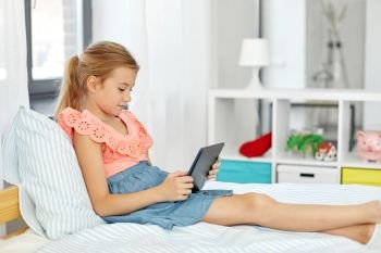 children, technology and communication concept - smiling girl with tablet computer sitting on bed at home. smiling girl with tablet pc sitting on bed at home