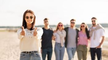 friendship, leisure and people concept - happy woman in sunglasses with group of friends on beach in summer showing thumbs up. woman with friends on beach showing thumbs up