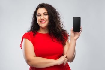 people and portrait concept - happy woman in red dress showing smartphone with blank screen over grey background. happy woman in red dress showing smartphone