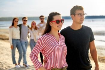 relationships and people concept - happy couple with group of friends hugging on beach in summer. happy friends walking along summer beach