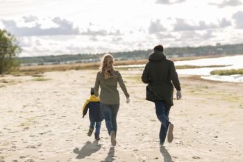 family, leisure and people concept - happy mother, father and little son running along autumn beach. happy family running along autumn beach