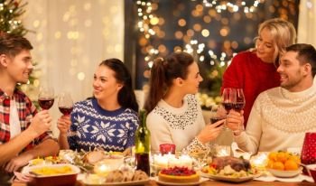 holidays and celebration concept - happy friends having christmas dinner at home, drinking red wine and clinking glasses. happy friends drinking red wine at christmas party