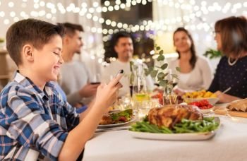 technology, holidays and people concept - happy boy with smartphone having family dinner party at home. boy with smartphone at family dinner party
