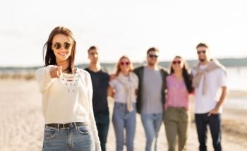 friendship, leisure and people concept - happy woman in sunglasses with group of friends on beach in summer pointing to you. happy woman with friends on beach pointing to you