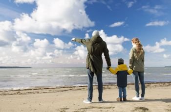 family, leisure and people concept - happy mother, father and little son at autumn beach looking at sea. happy family at autumn beach looking at sea