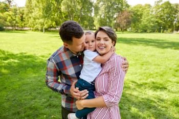 family, leisure and people concept - happy mother, father and little son hugging at summer park. happy family hugging at summer park