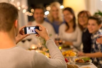 celebration, holidays and people concept - man with smartphone taking picture of family at dinner party. man taking picture of family at dinner party