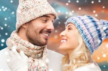 couple, christmas and holidays concept - smiling man and woman in hats and scarf over winter forest background. smiling couple in winter clothes hugging