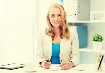 office, business, education, technology and internet concept - smiling businesswoman or student sitting at table and writing to notebook. businesswoman writing to notebook at office