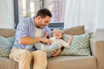 family, parenthood and fatherhood concept - happy laughing father tickling little baby daughter at home. happy father tickling little baby daughter at home