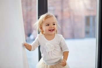 childhood, babyhood and people concept - happy smiling baby girl at home window. happy smiling baby girl at home window