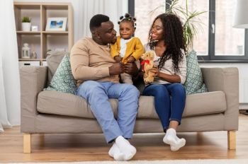 family, parenthood and people concept - happy african american mother and father with baby daughter sitting on sofa at home. happy african family with baby daughter at home