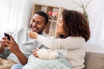 people and leisure concept - african american couple with popcorn and smartphone at home. african couple with popcorn and smartphone at home