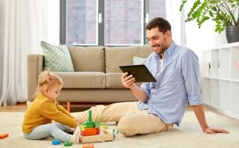 family, fatherhood and people concept - happy father with tablet pc computer and little baby daughter playing with wooden toy toy blocks kit at home. father with tablet pc and baby daughter at home