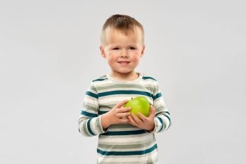 education, health and childhood concept - portrait of smiling little boy holding green apple over grey background. portrait of smiling boy holding green apple