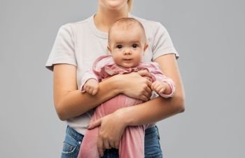 family, child and parenthood concept - happy smiling young mother holding little baby daughter over grey background. happy young mother holding little baby daughter