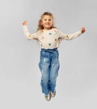 childhood, fashion and people concept - smiling little girl in jeans jumping over grey background. smiling little girl jumping