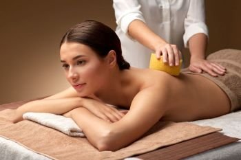 wellness, beauty and relaxation concept - beautiful young woman having back massage with sponge at spa. woman having back massage with sponge at spa