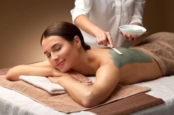 wellness, beauty and cosmetology concept - beautiful young woman lying with closed eyes and cosmetologist applying clay mask by spatula at spa. woman and cosmetologist applying clay mask in spa