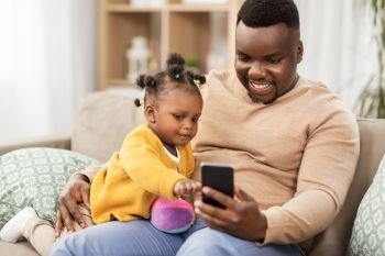 family, fatherhood and technology concept - african american father with smartphone and little baby daughter playing with ball at home. father with smartphone and baby daugter at home