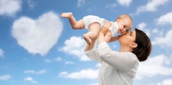 family, child and parenthood concept - happy smiling middle-aged mother kissing little baby daughter over blue sky and heart shaped cloud background. happy mother kissing little baby daughter