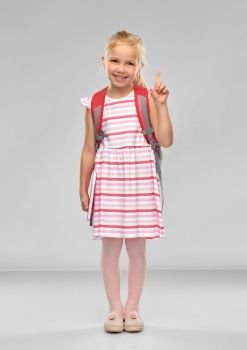 childhood, education and people concept - happy student girl with school bag pointing finger up over grey background. little girl with school bag pointing finger up