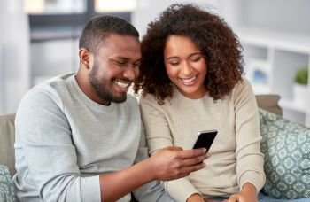 technology, internet and people concept - happy african american couple with smartphone at home. african american couple with smartphone at home