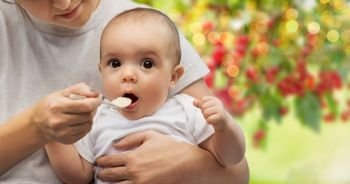 child, eating and food concept - close up of mother with spoon feeding little baby over summer garden background. close up of mother with spoon feeding little baby