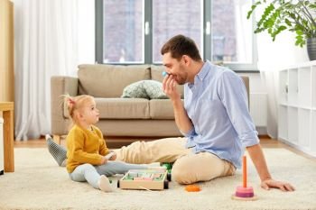family, fatherhood and people concept - happy father and little baby daughter playing with wooden toy toy blocks kit at home. father playing with little baby daughter at home