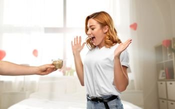 relationships, holiday and valentine’s day concept - happy woman in white t-shirt receiving little gift box from man over bedroom decorated with heart shaped balloons background. happy couple with gift on valentines day at home