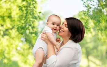 family, child and parenthood concept - happy smiling middle-aged mother holding little baby daughter over green natural background. happy middle-aged mother with little baby daughter