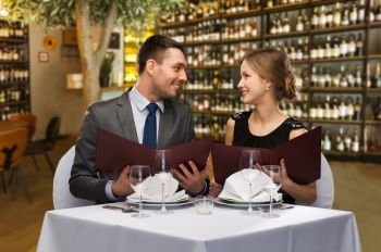 leisure and luxury concept - smiling couple with menus over restaurant or wine bar background. happy couple with menus at restaurant or wine bar