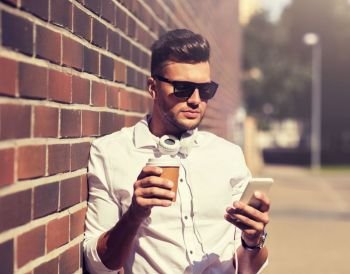 technology and people concept - young man in sunglasses with smartphone and coffee cup on city street. man with smartphone and coffee cup on city street