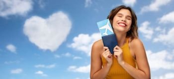 travel, tourism and vacation concept - happy smiling young woman in mustard yellow top with air ticket and passport over blue sky and clouds background. happy young woman with air ticket and passport