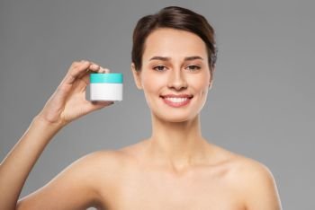 beauty, cosmetics and skincare concept - happy young woman holding jar of cream over grey background. happy young woman holding jar of cream