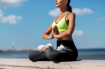 fitness, sport and yoga concept - young woman meditating in lotus pose at seaside. young woman meditating in lotus pose at seaside