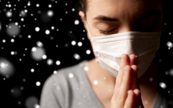 health protection, safety and pandemic concept - sick young woman in protective medical face mask praying over snow on black background in winter. sick young woman in protective face mask praying