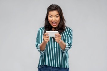 technology and people concept - surprised asian woman using smartphone over grey background. surprised asian woman using smartphone