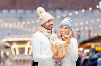 winter holidays and people concept - happy couple with gift box over christmas market background. smiling couple in winter clothes with gift box