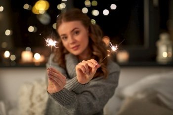 christmas, holiday and people concept - happy young woman with sparklers in bed at home bedroom at night. happy young woman with sparklers in bed at home