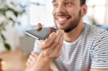 technology, remote job and people concept - close up of happy smiling man calling on smartphone or using voice command recorder at home office. man calling or recording voice with phone at home