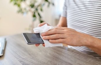 remote job, business and disinfection concept - close up of man cleaning smartphone with antiseptic wet wipe at home office. man cleaning phone with wet wipe at home office