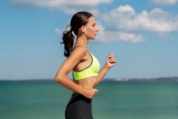 fitness, sport and healthy lifestyle concept - young woman with wireless earphones running at seaside. woman with wireless earphones running at seaside
