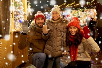 family, winter holidays and celebration concept - happy mother, father and little daughter waving hands at christmas market on town hall square in tallinn, estonia over snow. happy family waving hands at christmas market