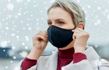 health, safety and pandemic concept - young woman wearing black face protective reusable barrier mask outdoors over snow. woman wearing protective reusable barrier mask