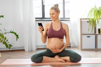 yoga, sport and people concept - happy pregnant woman with smartphone at home. pregnant woman with smartphone doing yoga at home