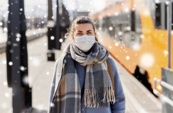 health safety, travel and pandemic concept - young woman in protective face mask at empty railway station over snow. woman in protective face mask at railway station