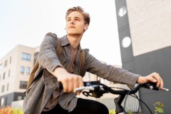 lifestyle, transport and people concept - young man or teenage student boy with earphones and backpack riding bicycle in city. teenage boy with earphones and bag riding bicycle