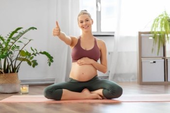 fitness, sport and people concept - happy pregnant woman showing thumbs up sitting on yoga mat at home. pregnant woman shows thumbs up sitting on yoga mat