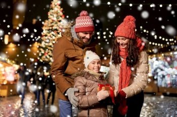 family, winter holidays and celebration concept - happy mother, father and little daughter with gift at christmas market on town hall square in tallinn, estonia over snow. happy family with gift at christmas market in city